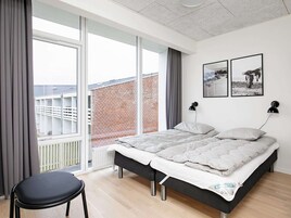 Un dormitorio moderno con una cama grande, una silla y vista a un edificio de ladrillo a través de un ventanal.