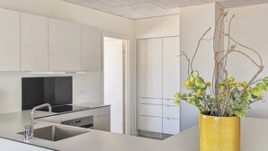A modern kitchen with white cabinets, a stainless steel sink, and a yellow vase with flowers. - 5 Star Holiday Home in Ringkobing (Ringkobing)