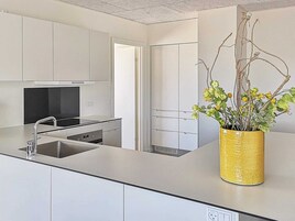 Una cocina moderna con armarios blancos, un lavamanos de acero inoxidable y un jarrón amarillo con flores.