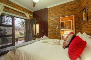 A hotel room with a large bed, a red throw blanket, and a view of the outdoors through a glass door. - Doringpoort Safari Lodge (Nkomazi)