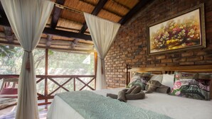 A bedroom with a large bed, a painting on the wall, and a view of the outdoors. - Doringpoort Safari Lodge (Nkomazi)