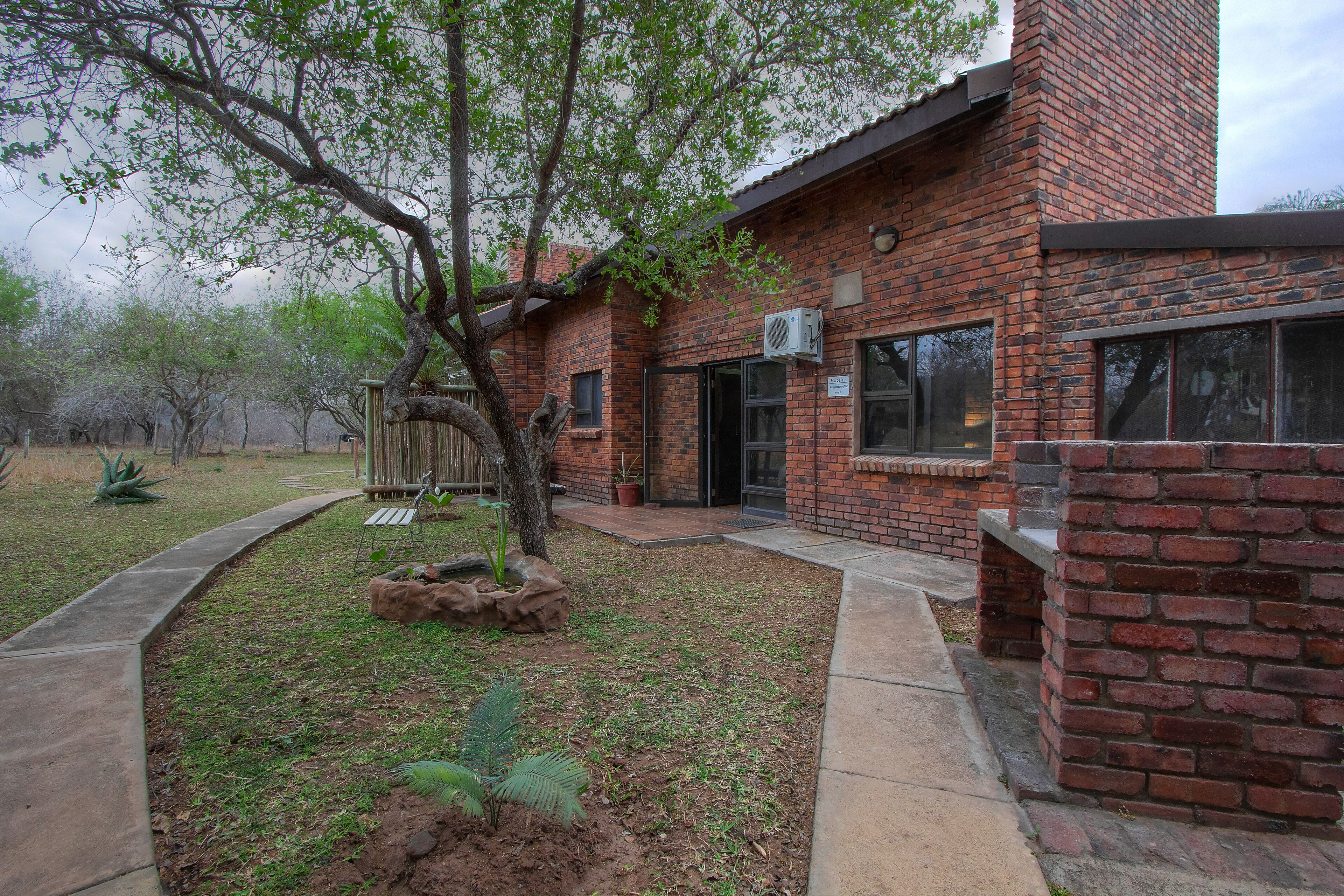 A brick house with a covered patio, a tree, and a small garden area.