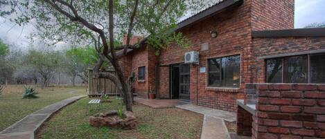 A brick house with a covered patio, a tree, and a small garden area.