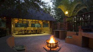 An outdoor seating area with a fire pit, a thatched-roof structure, and a staircase leading to an upper level. - Doringpoort Safari Lodge (Nkomazi)