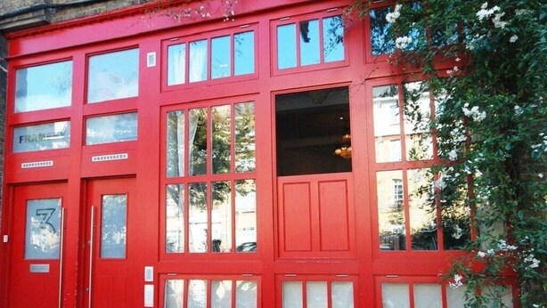 A red building with multiple windows and a door, surrounded by greenery and flowers. - Framery 3 - Funky studio in trendy Shoreditch (London)