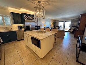 A modern kitchen with a central island, built-in appliances, and a dining area with wicker chairs.