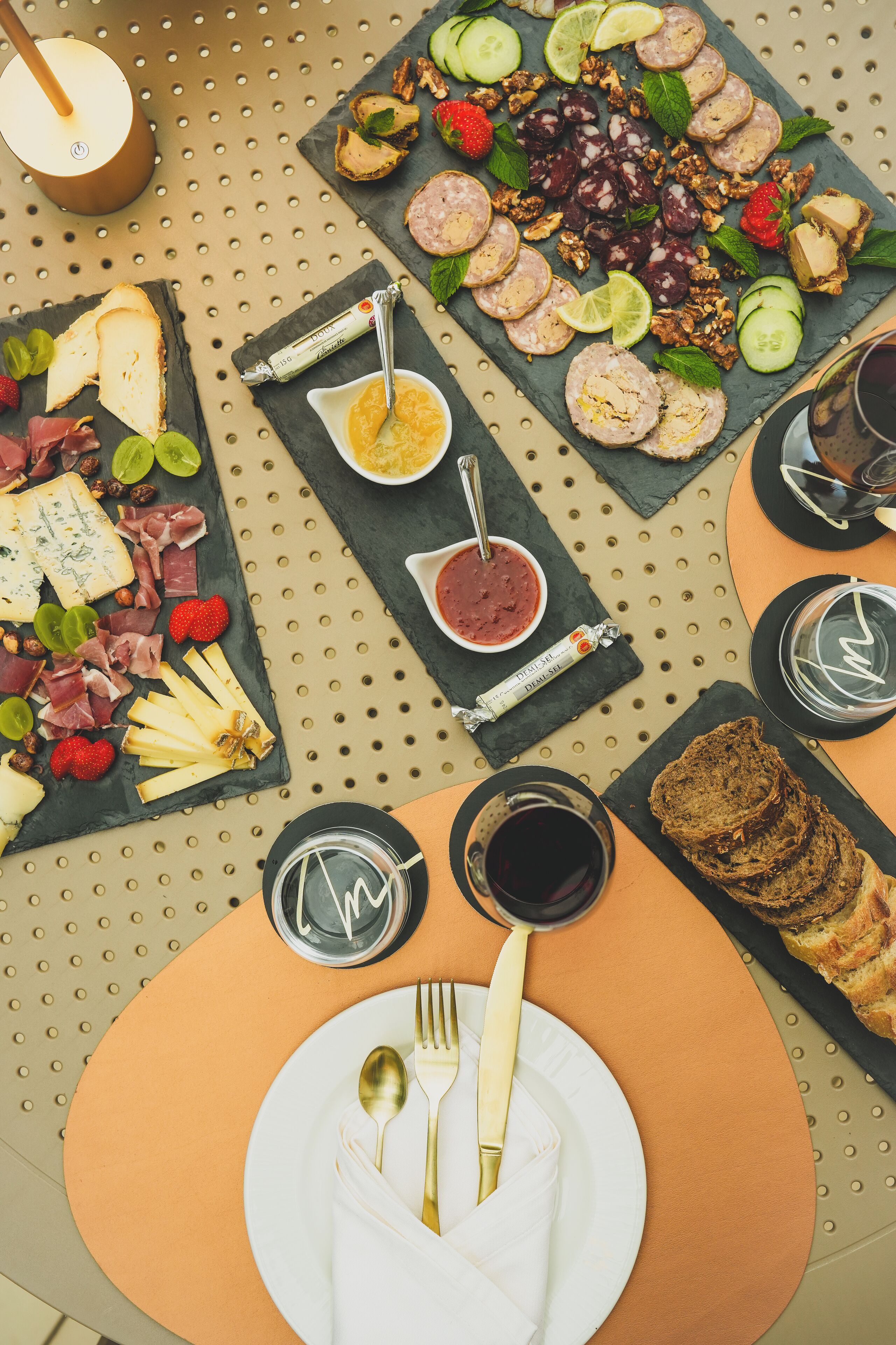 A table set with various cheeses, meats, and fruits, accompanied by glasses of wine and a candle.
