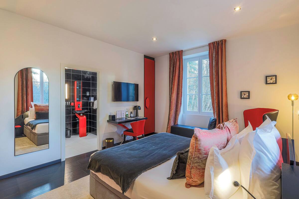 A modern hotel room with a large bed, a desk, a TV, and a window with curtains.
