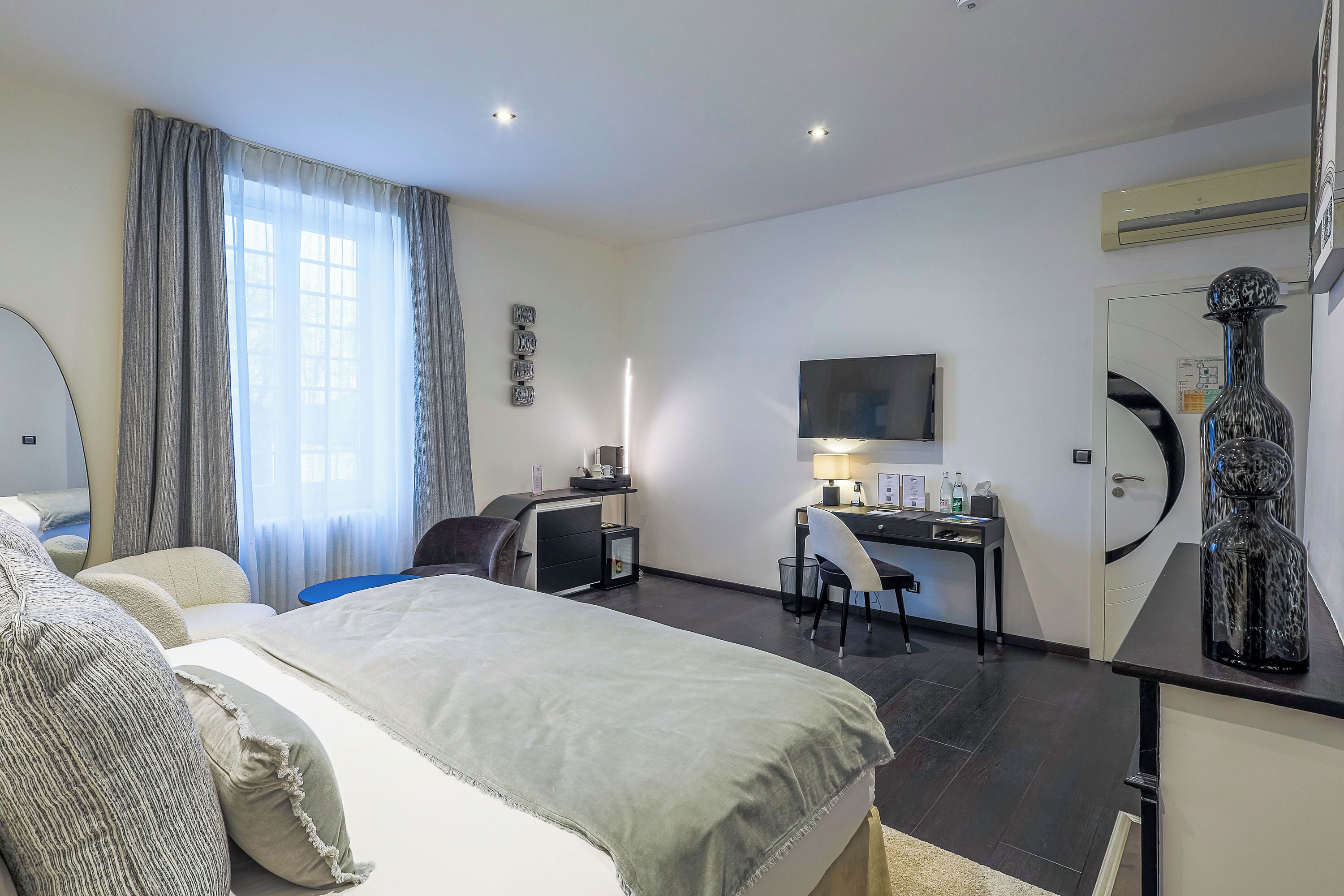 Une chambre d’hôtel équipée d’un lit, d’un bureau, d’une chaise, d’un miroir et d’une grande fenêtre avec des rideaux.