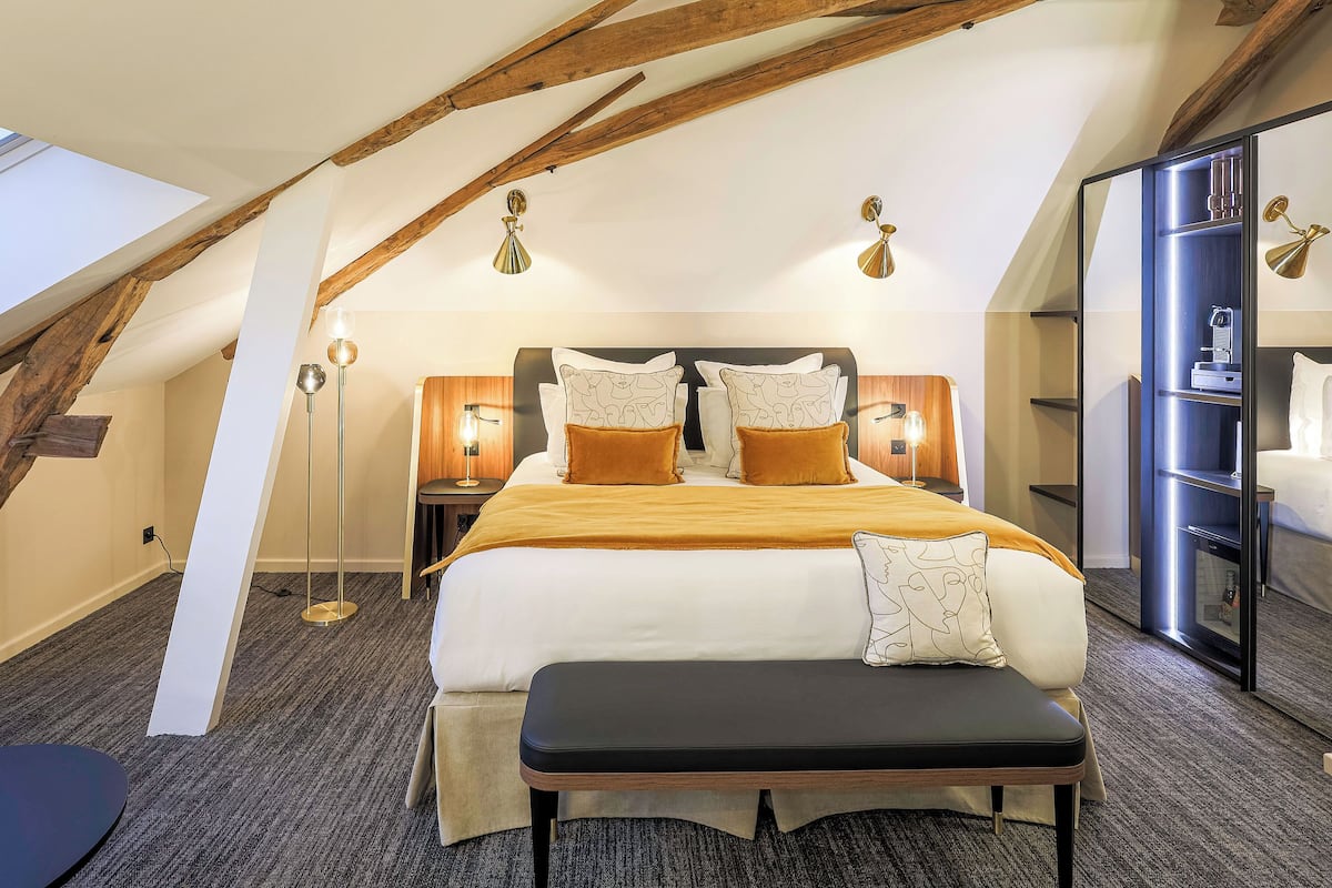 A modern bedroom with a large bed, a bench, and a wardrobe.