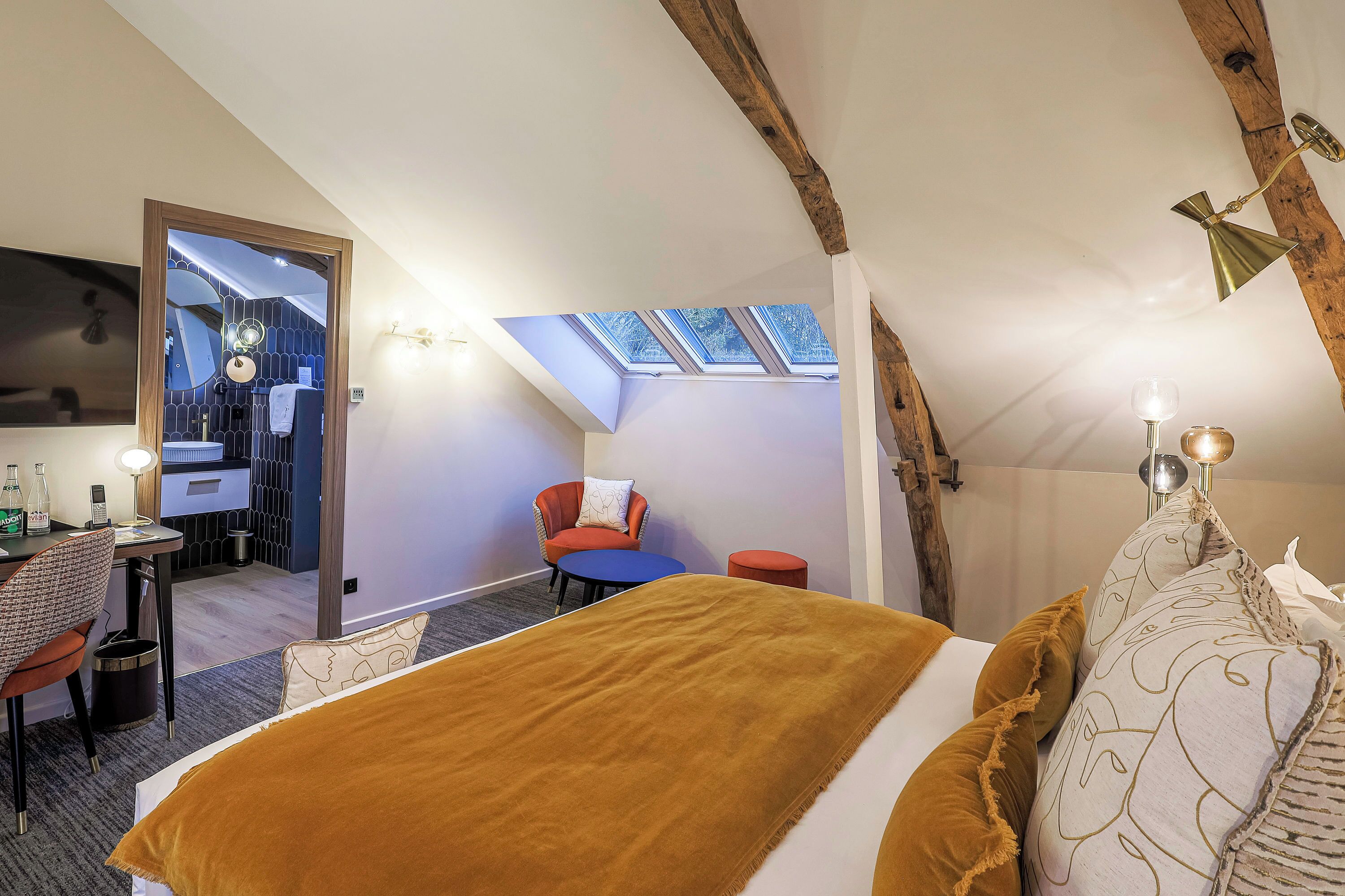 A bedroom with a bed, a desk, a chair, a small table, and a skylight.