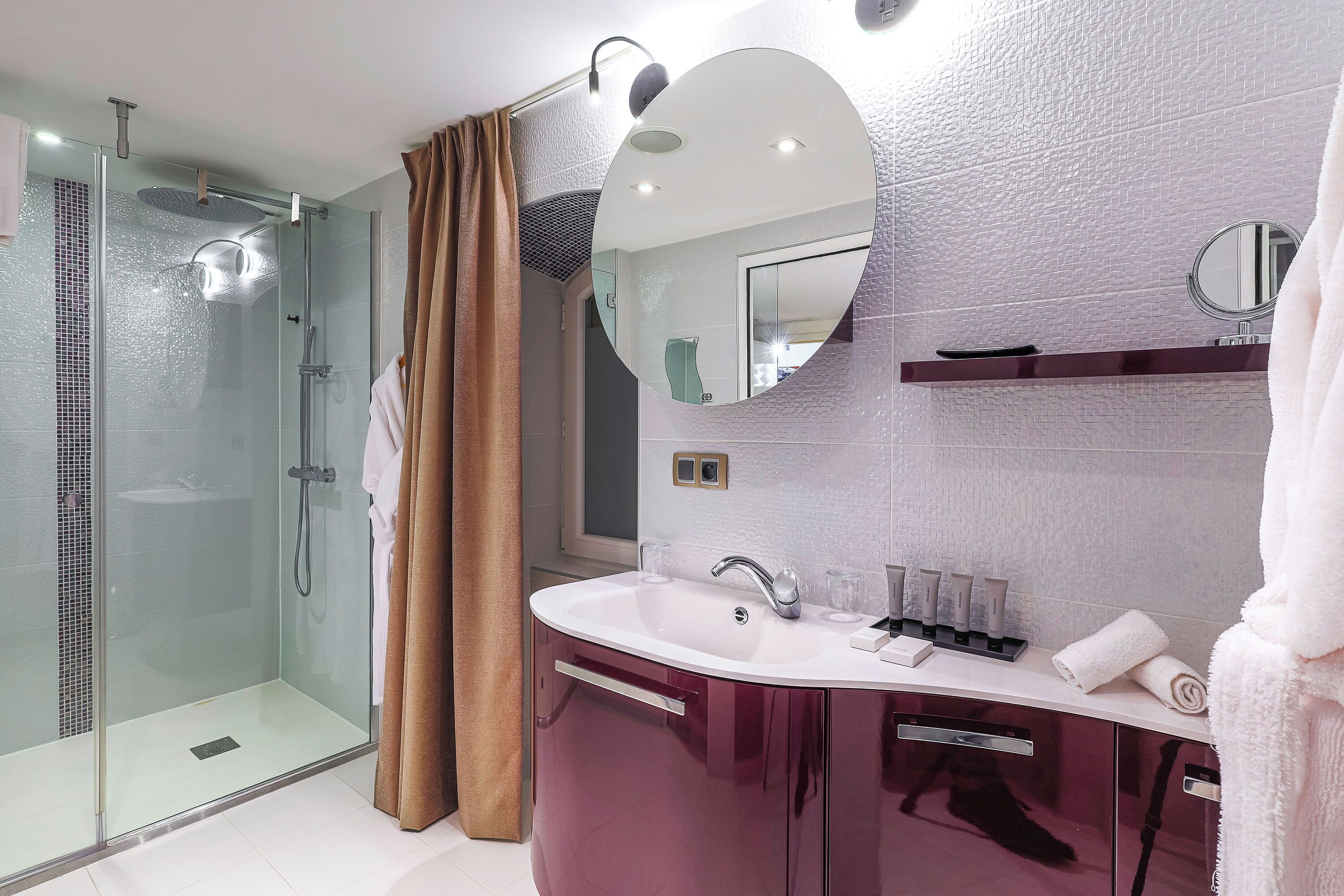 A modern bathroom with a glass-enclosed shower, a vanity with a large mirror, and a white sink.
