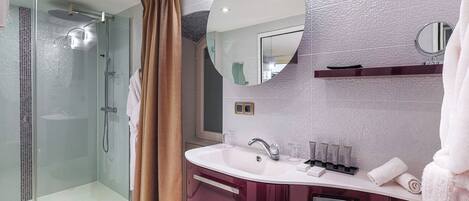 Un baño moderno con ducha de vidrio, tocador con un espejo grande y un lavamanos blanco.
