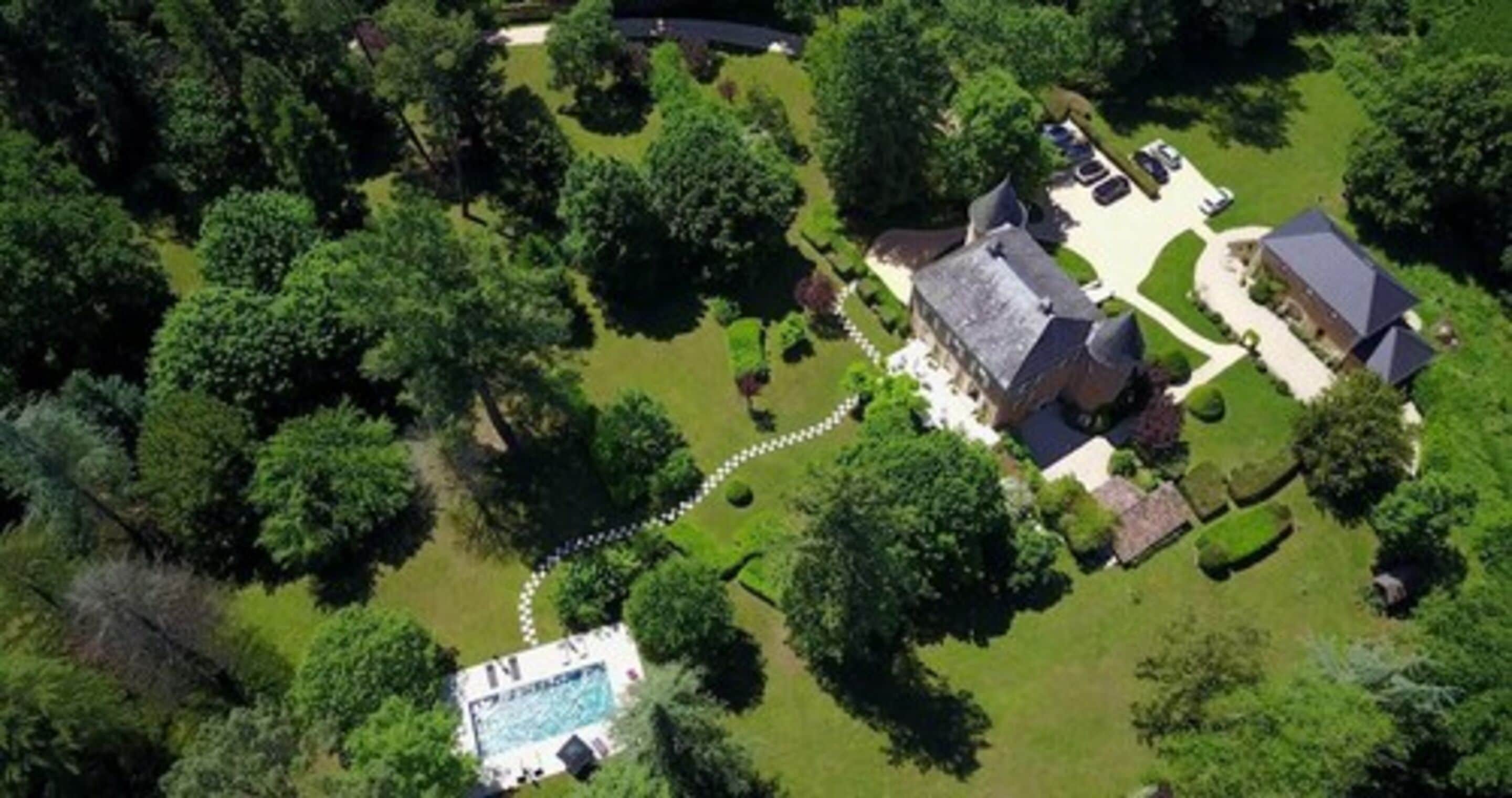 An aerial view of a property with a swimming pool, a large house, and surrounding greenery.