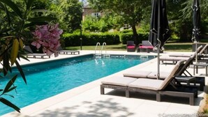 Une piscine entourée de verdure et d’arbres, avec des chaises longues et des parasols.