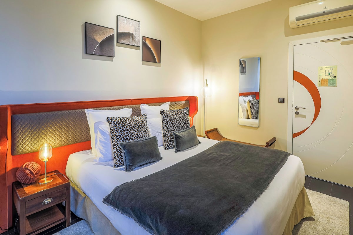A neatly made bed with a headboard, a bedside lamp, and a nightstand with a drawer.