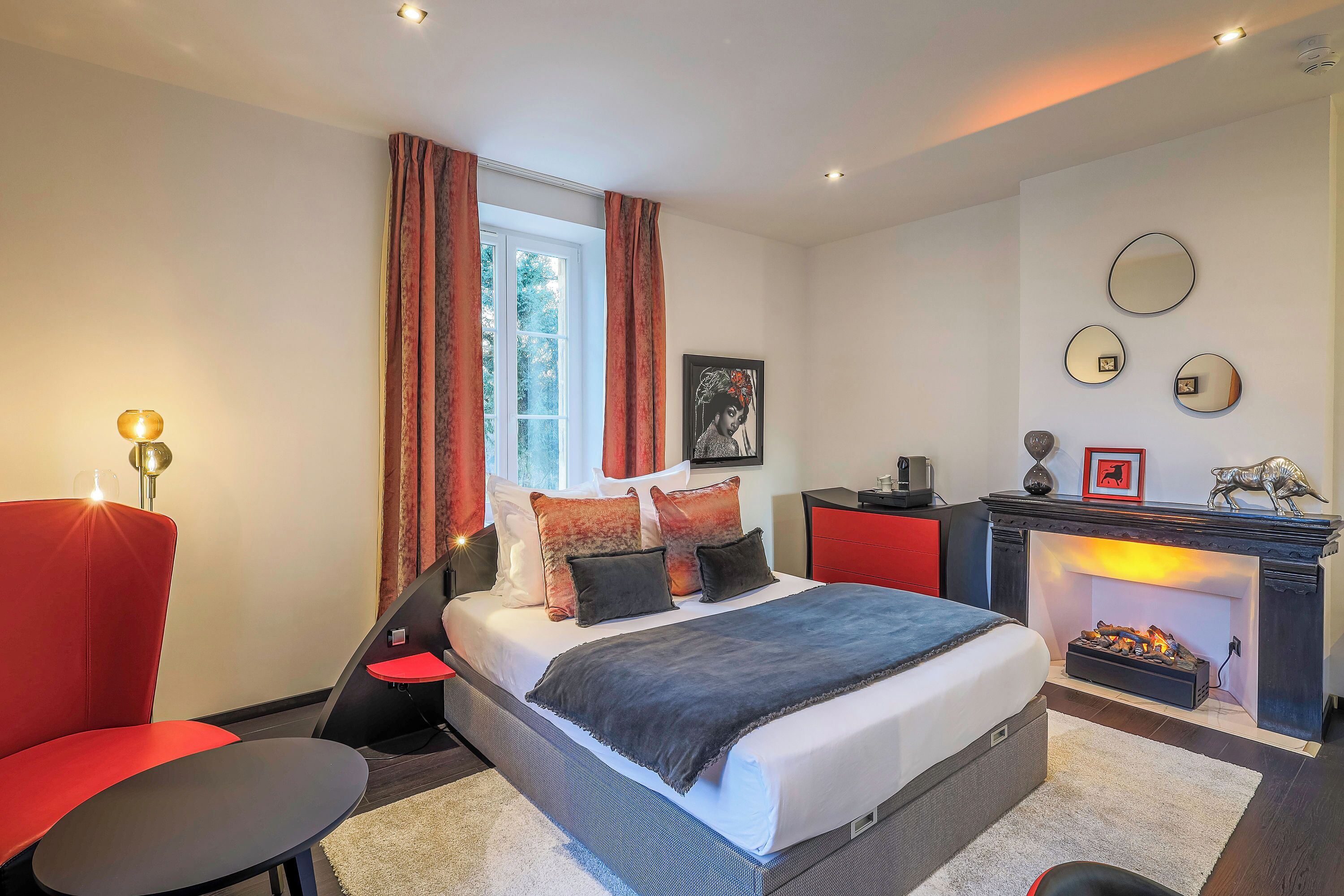 A modern bedroom with a large bed, a fireplace, and a red accent chair.