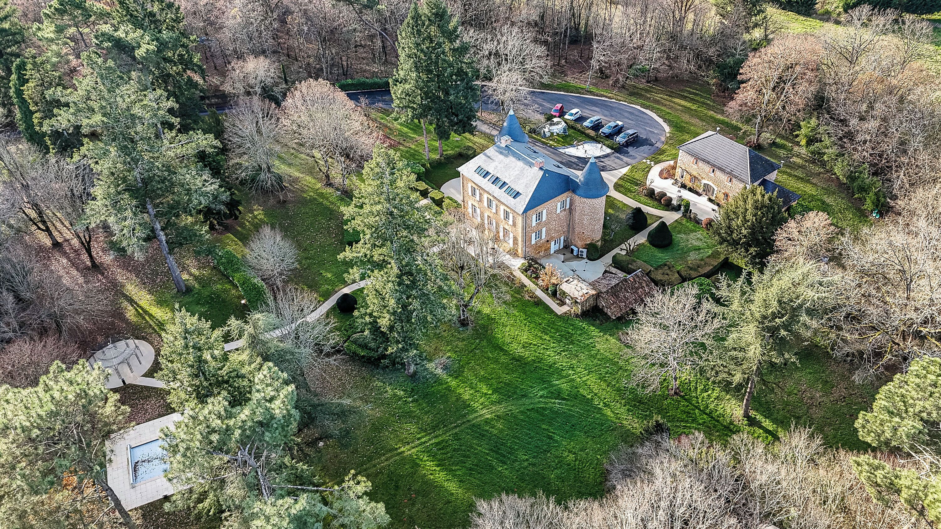 An aerial view of a large building with a distinctive blue roof, surrounded by lush greenery and trees.