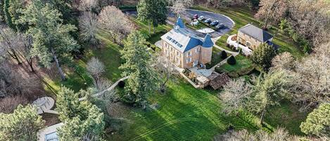 An aerial view of a large building with a distinctive blue roof, surrounded by lush greenery and trees.