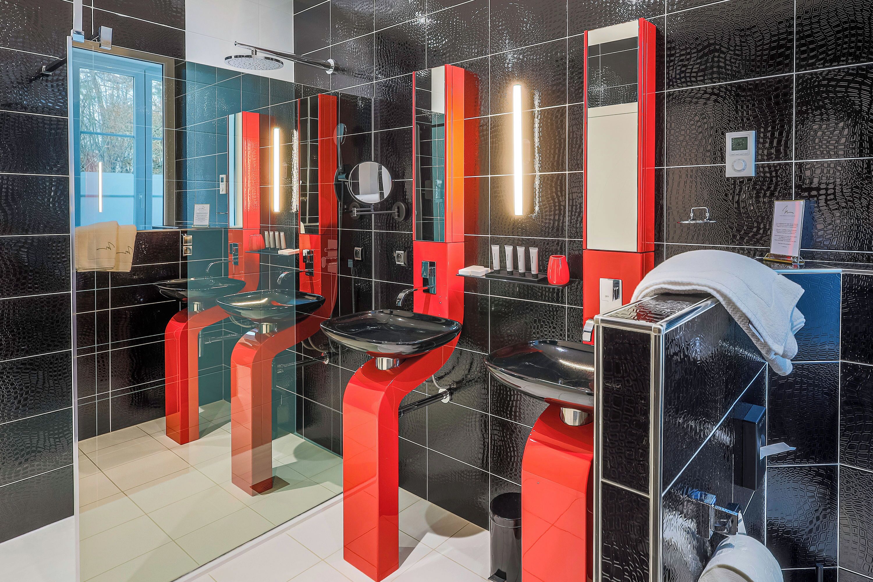 A modern bathroom with black and red tiled walls, a glass shower enclosure, and a white sink.