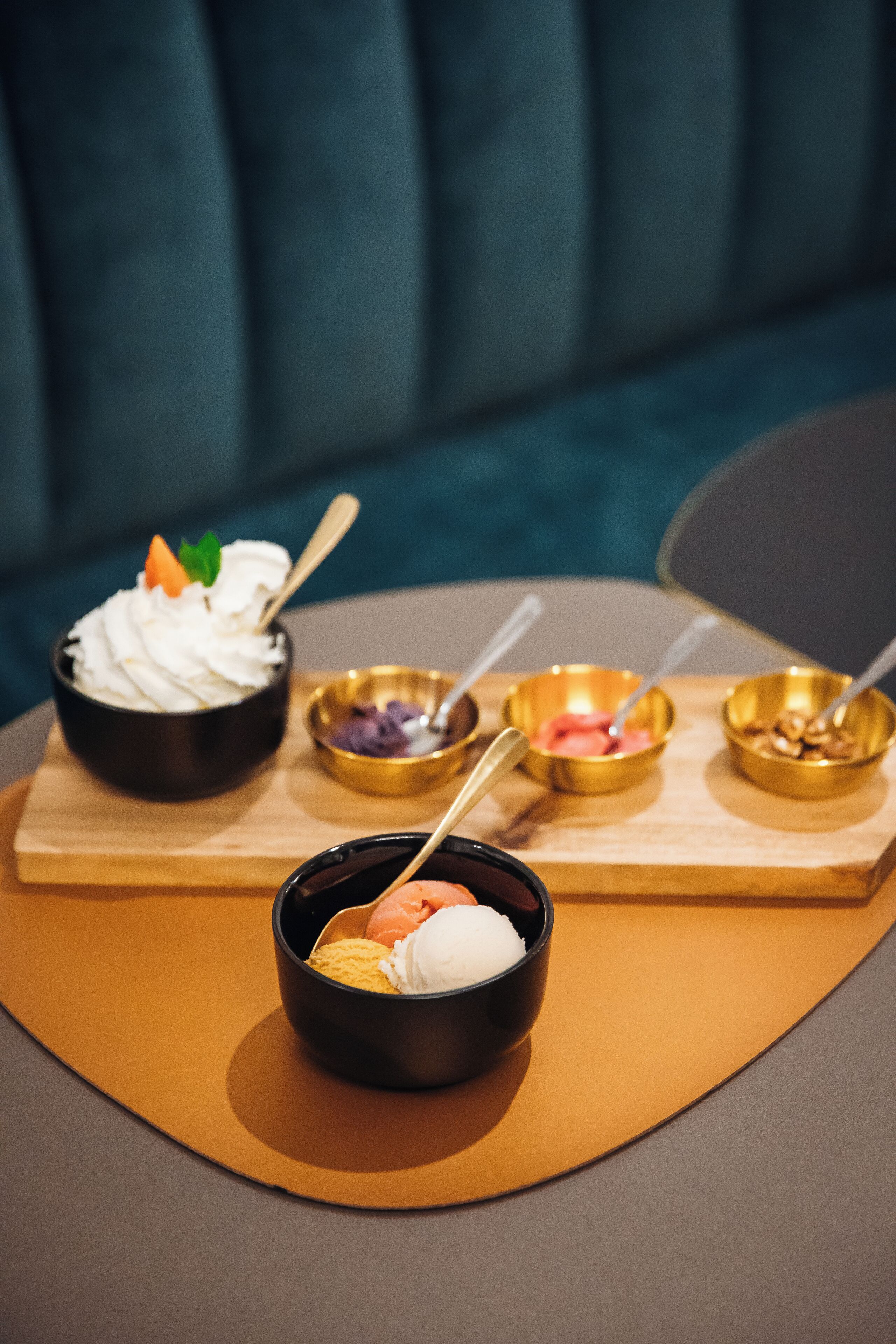 Een desserttafel met diverse schalen ijs en toppings, geplaatst op een houten dienblad.