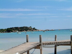 A wooden pier extending into a calm sea with boats and a rocky island in the background.
