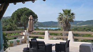 Une terrasse extérieure aménagée avec des meubles en osier, une pergola et une vue sur un paysage côtier.