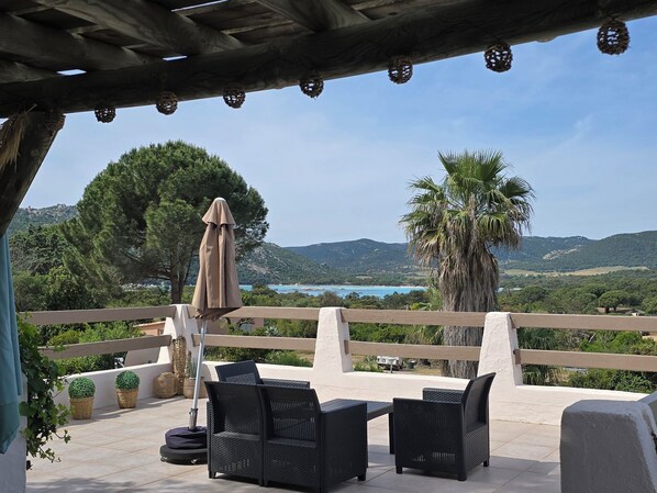 An outdoor patio with wicker furniture, a pergola, and a view of a coastal landscape.