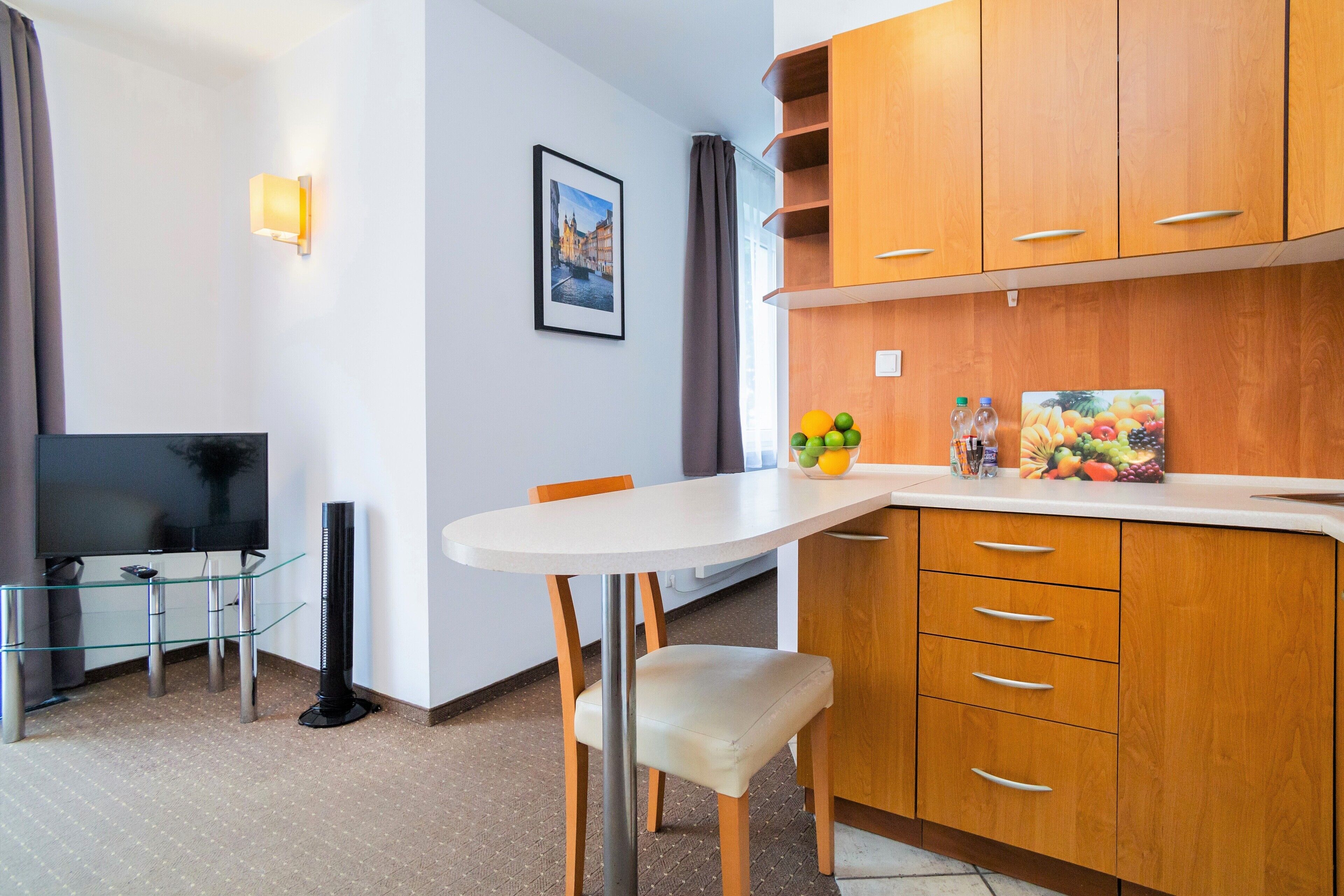 Una habitación de hotel compacta con comedor, televisión de pantalla plana, armarios de madera y una pequeña mesa.