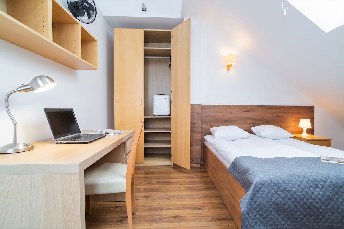 Une chambre à coucher de taille modeste, avec un bureau en bois, un ordinateur portable et un lit doté d’une tête de lit.