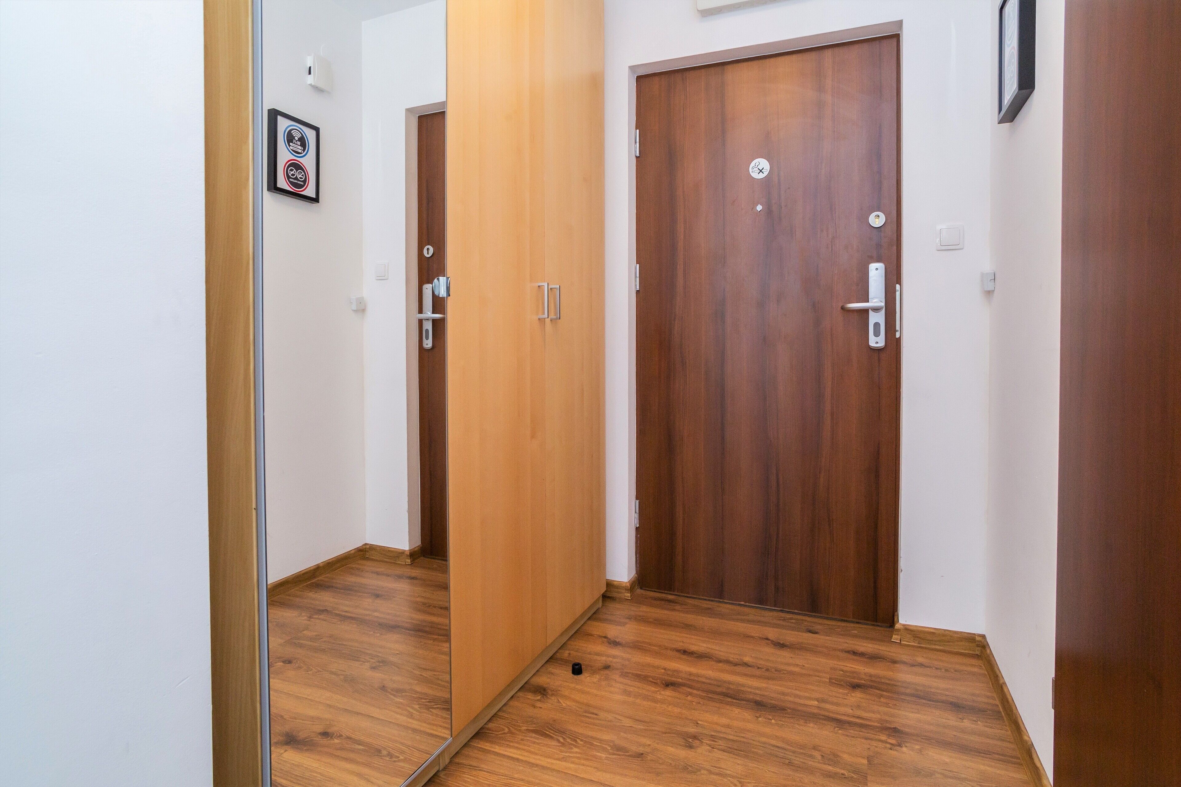 A hallway with wooden flooring, two wooden doors, and a small framed picture on the wall.
