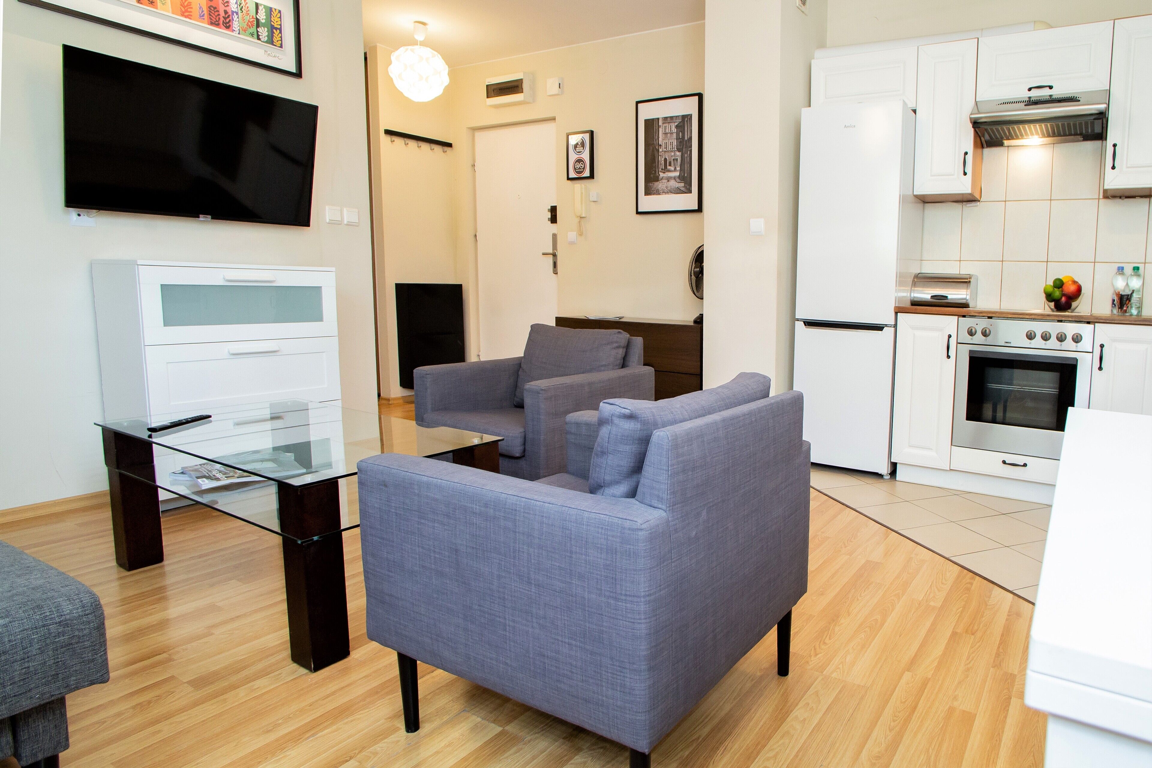 A modern living room with a grey sofa, a glass coffee table, and a flat-screen TV mounted on the wall.