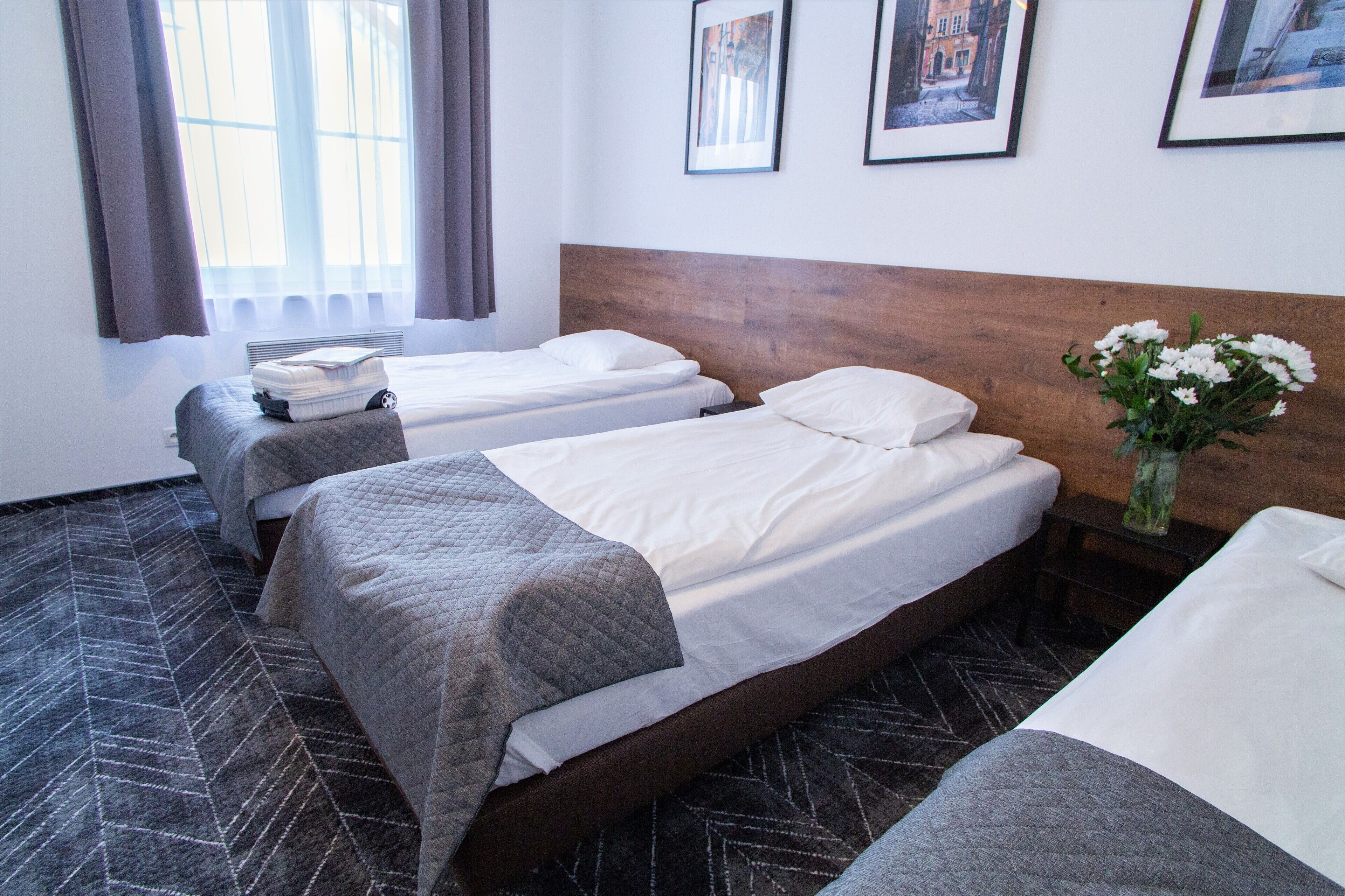 A hotel room with two beds, a wooden headboard, a window with curtains, and a framed picture on the wall.