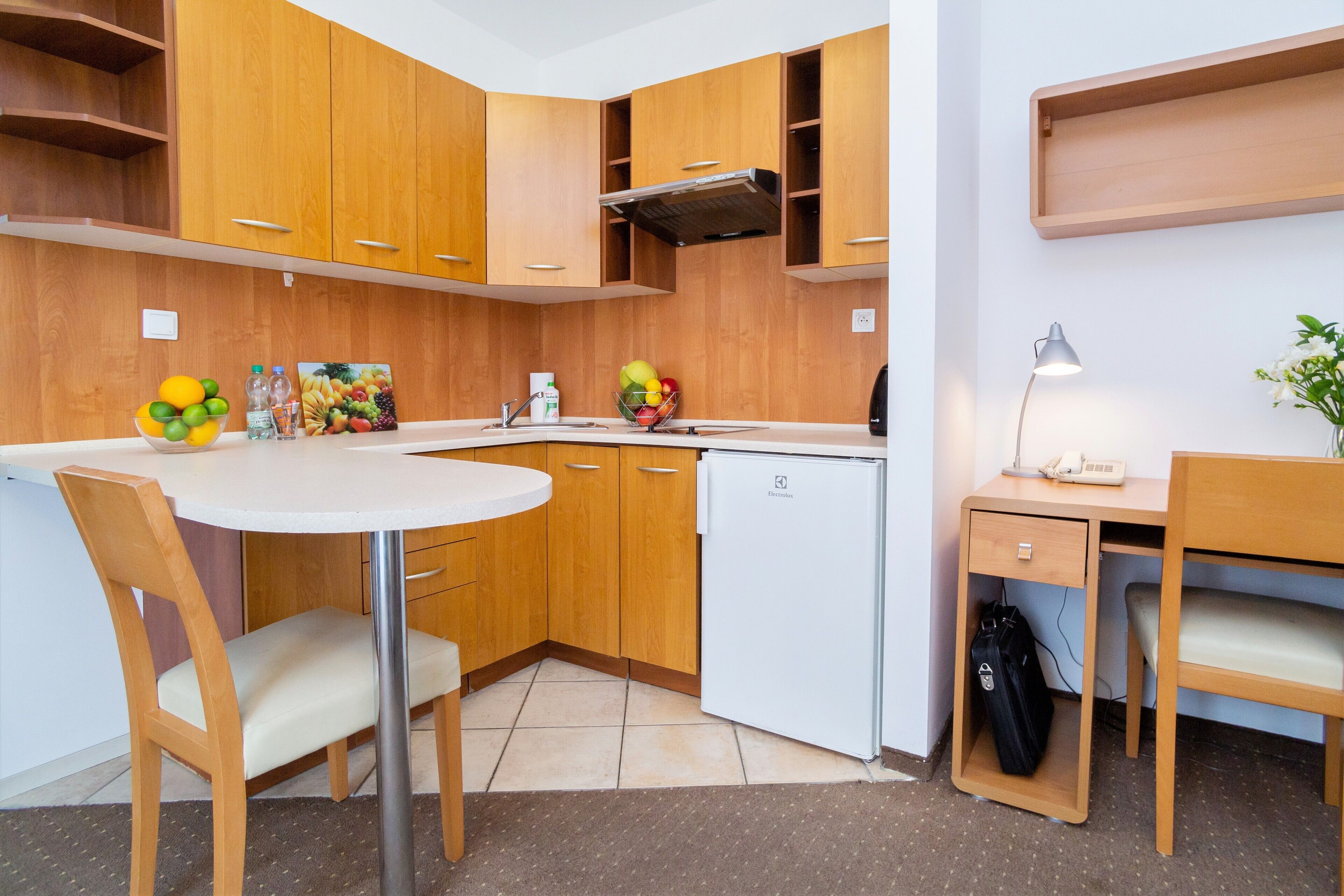 Une cuisine de taille réduite, avec des meubles en bois, un plan de travail blanc, un évier et un petit réfrigérateur.