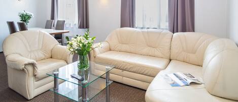 Een moderne woonkamer met een beige bank, een glazen salontafel, en een eethoek met een tafel en stoelen.