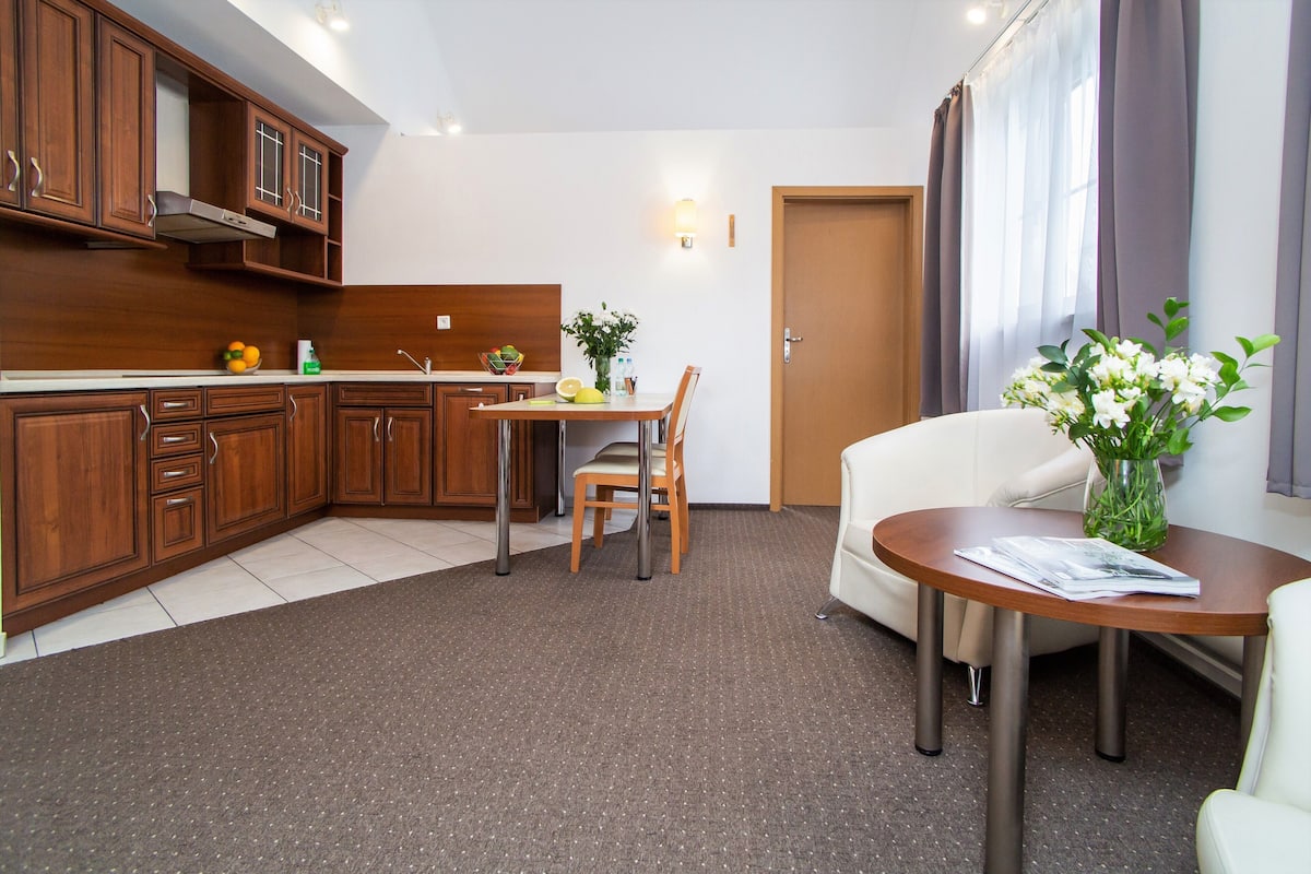Une cuisine compacte avec des meubles de rangement en bois, une table à manger avec des chaises et une petite table ronde ornée d’un vase de fleurs.