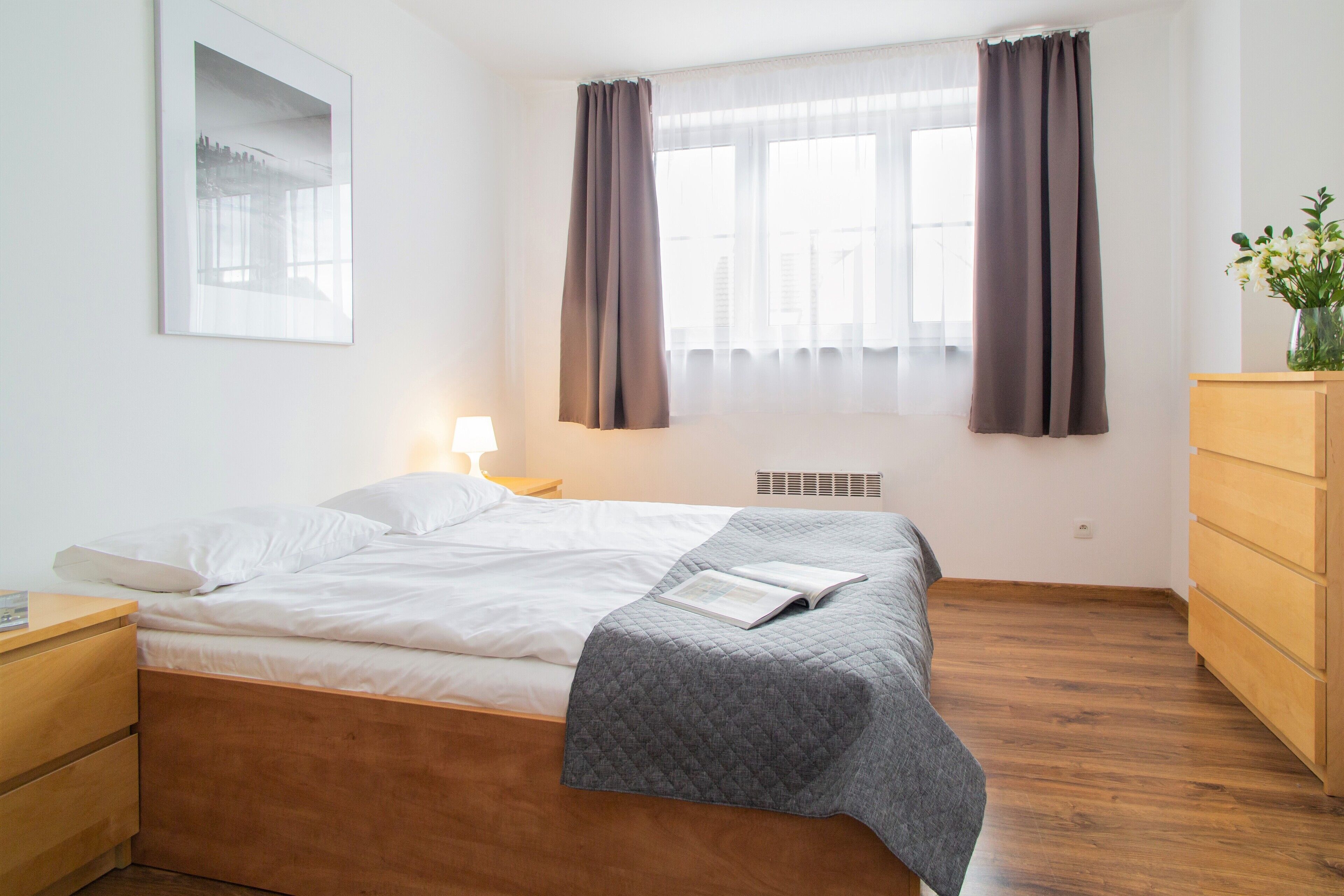 A bedroom with a bed, a bedside table, a dresser, and a window with curtains.