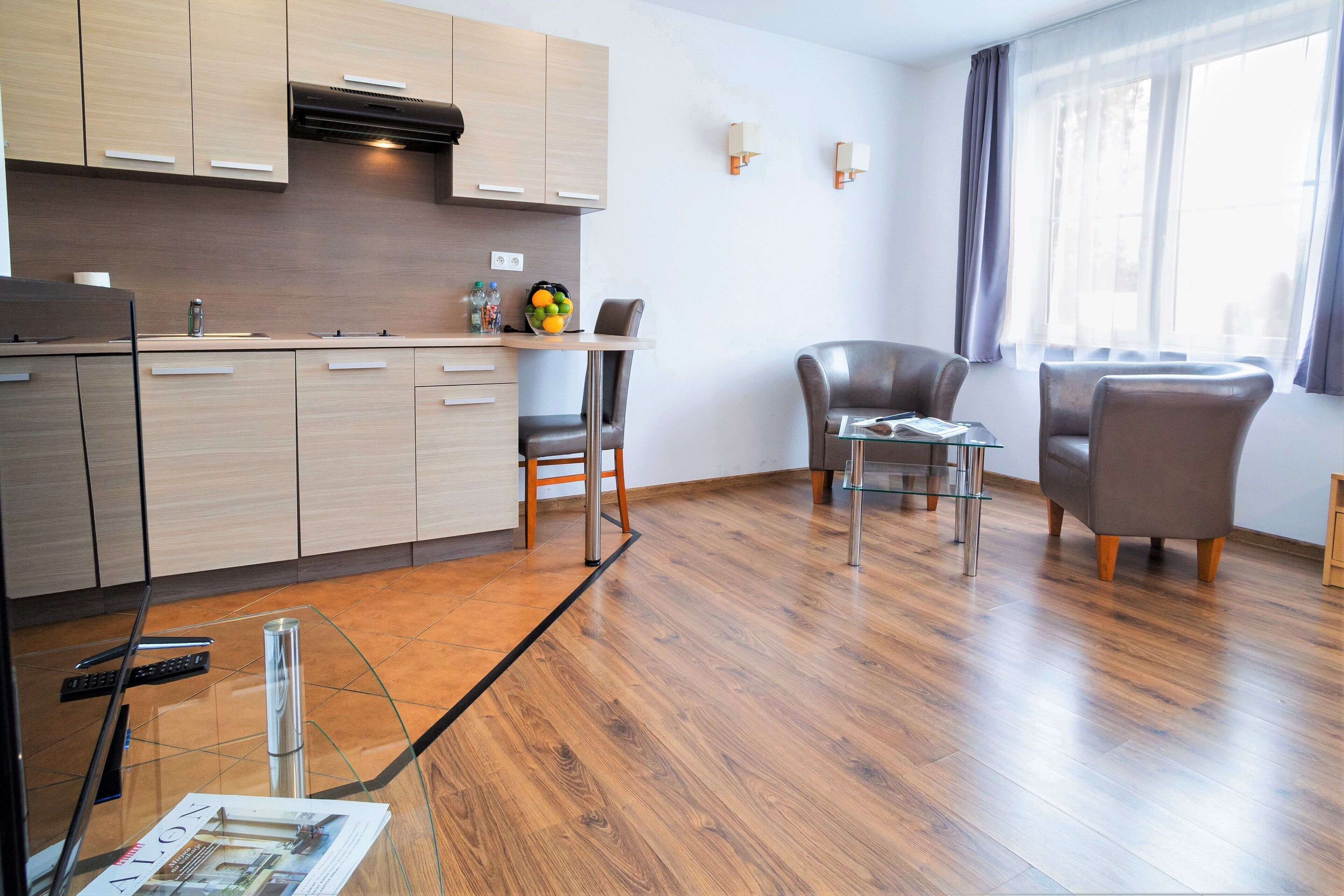 Una cocina moderna con armarios de madera, un comedor con mesa y sillas de vidrio, y un ventanal con cortinas.