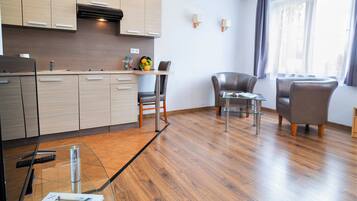 Una cocina moderna con armarios de madera, un comedor con mesa y sillas de vidrio, y un ventanal con cortinas.