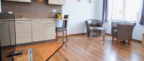 A modern kitchen with wooden cabinets, a dining area with a glass table and chairs, and a large window with curtains.