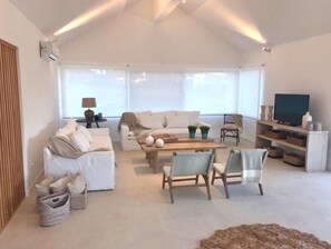 Relax in this spacious living room with a high ceiling and large windows, featuring a comfortable sofa set, coffee table, and television.