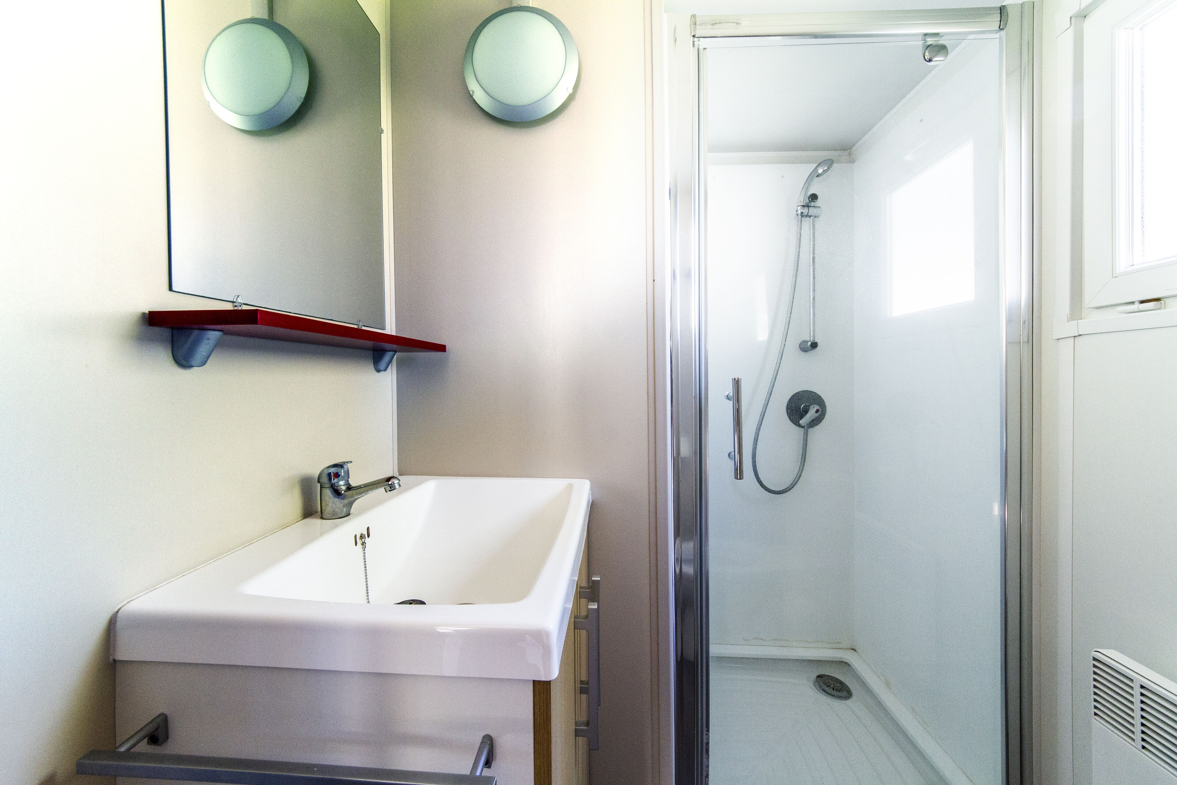 A bathroom with a white sink, a mirror, and a shower enclosure.