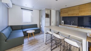 A modern kitchen with a central island, bar stools, and a built-in microwave. - Camping de Pujol (Argelès-sur-Mer)
