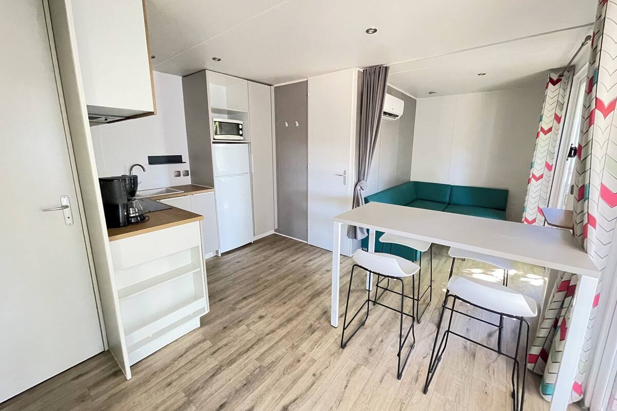 Um espaço compacto com cozinha americana, área de refeições com mesa e cadeiras, e um sofá verde.