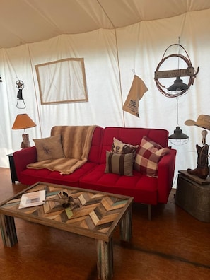Un canapé rouge avec une couverture et des coussins, une table basse en bois sur laquelle sont posés des papiers, et une lampe suspendue.