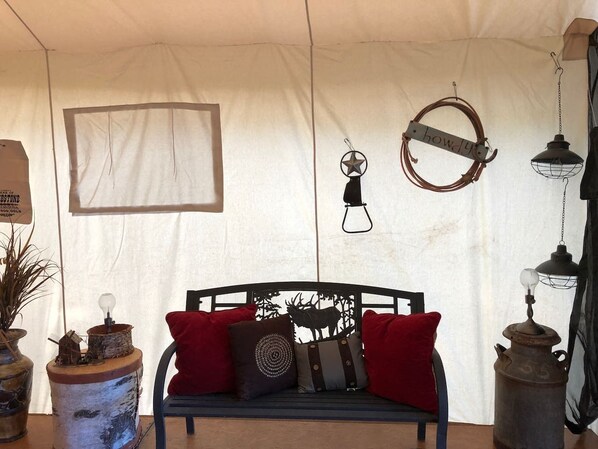 A tented room with a black metal bed, red and gray pillows, a star-shaped hanging light, and rustic decor items.