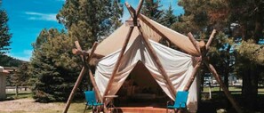 A tent with a simple structure, two chairs, and a table in an outdoor setting.