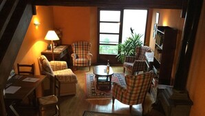 A cozy living room with a fireplace, plaid chairs, a coffee table, and a large window with a view of greenery.