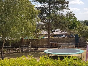 A trampoline in a fenced outdoor area with a stone wall and trees.