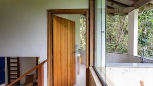 A wooden door leading to a bathroom with a white sink and a view of a balcony with greenery. - Casa Iporanga (Guarujá)